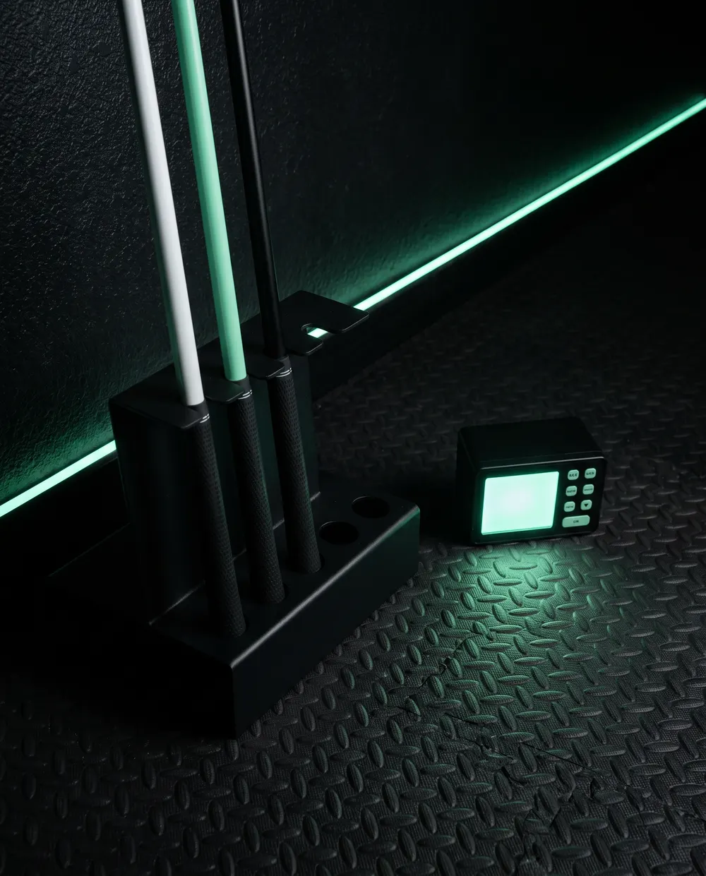 Three weighted speed-training shafts in a rack beside a radar swing-speed unit under mint edge light