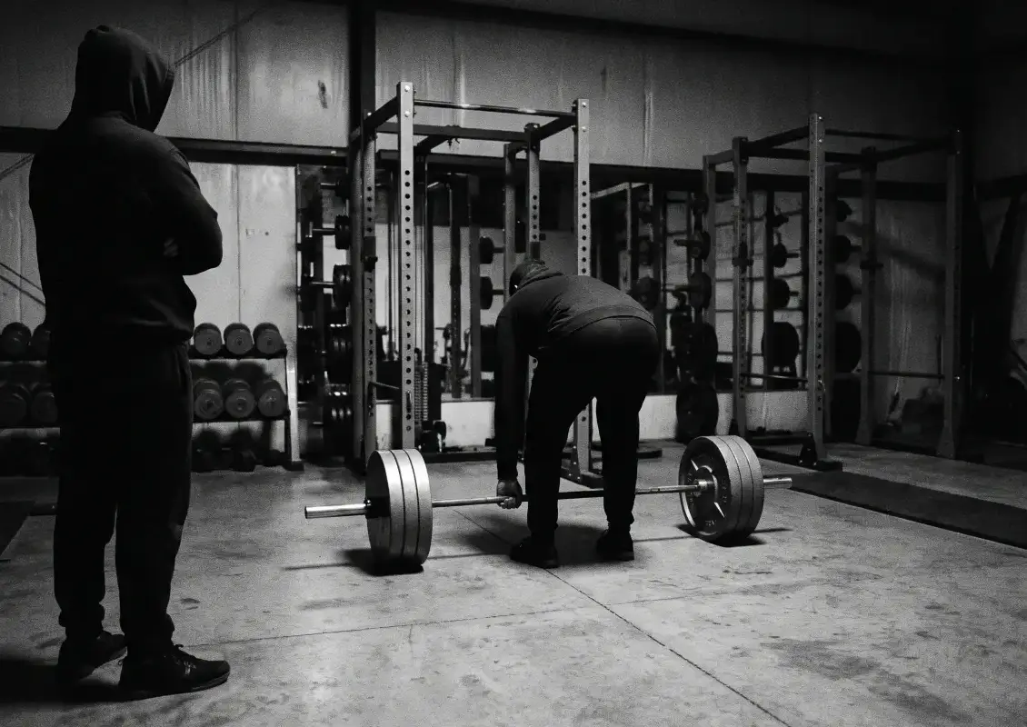 A coach watches a lifter set up at the bar