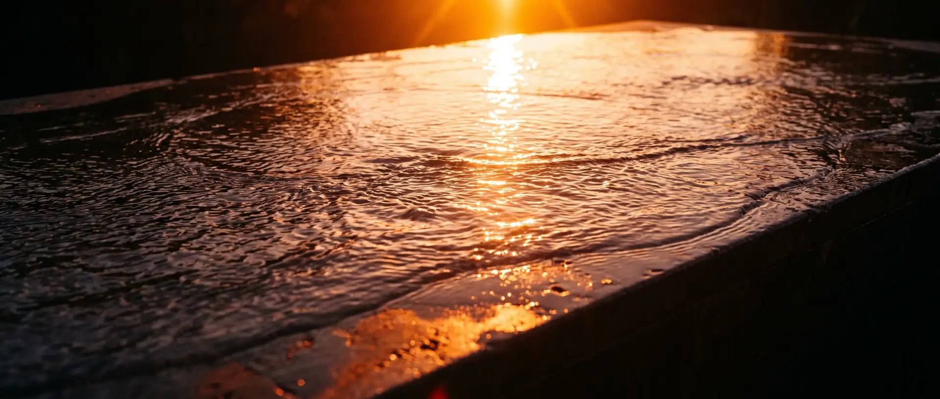 Water sheeting across dark wet stone with a blazing low sun reflected in it