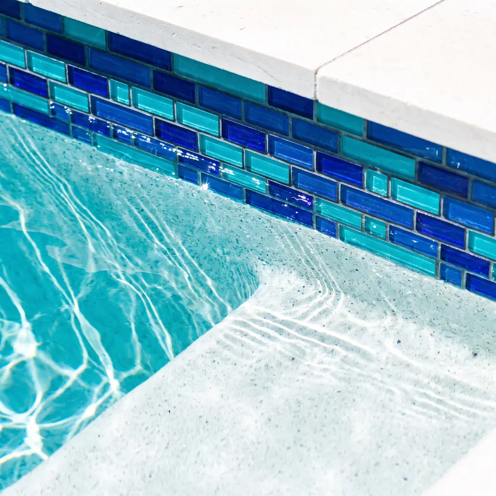 Close-up of new cobalt and turquoise glass waterline tile above a white quartz pool finish