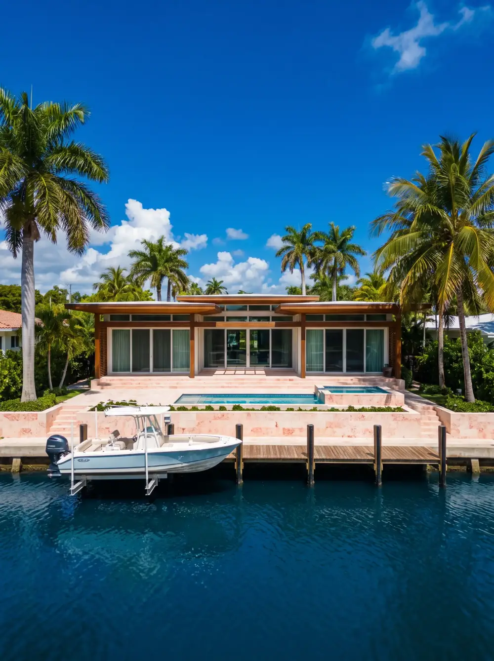 A low coastal-modern house with a coral stone terrace and a boat lift