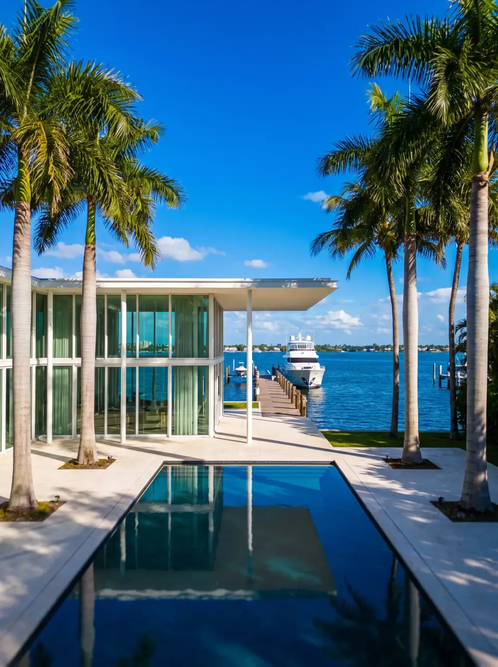 A glass pavilion house with a courtyard pool and a long yacht dock