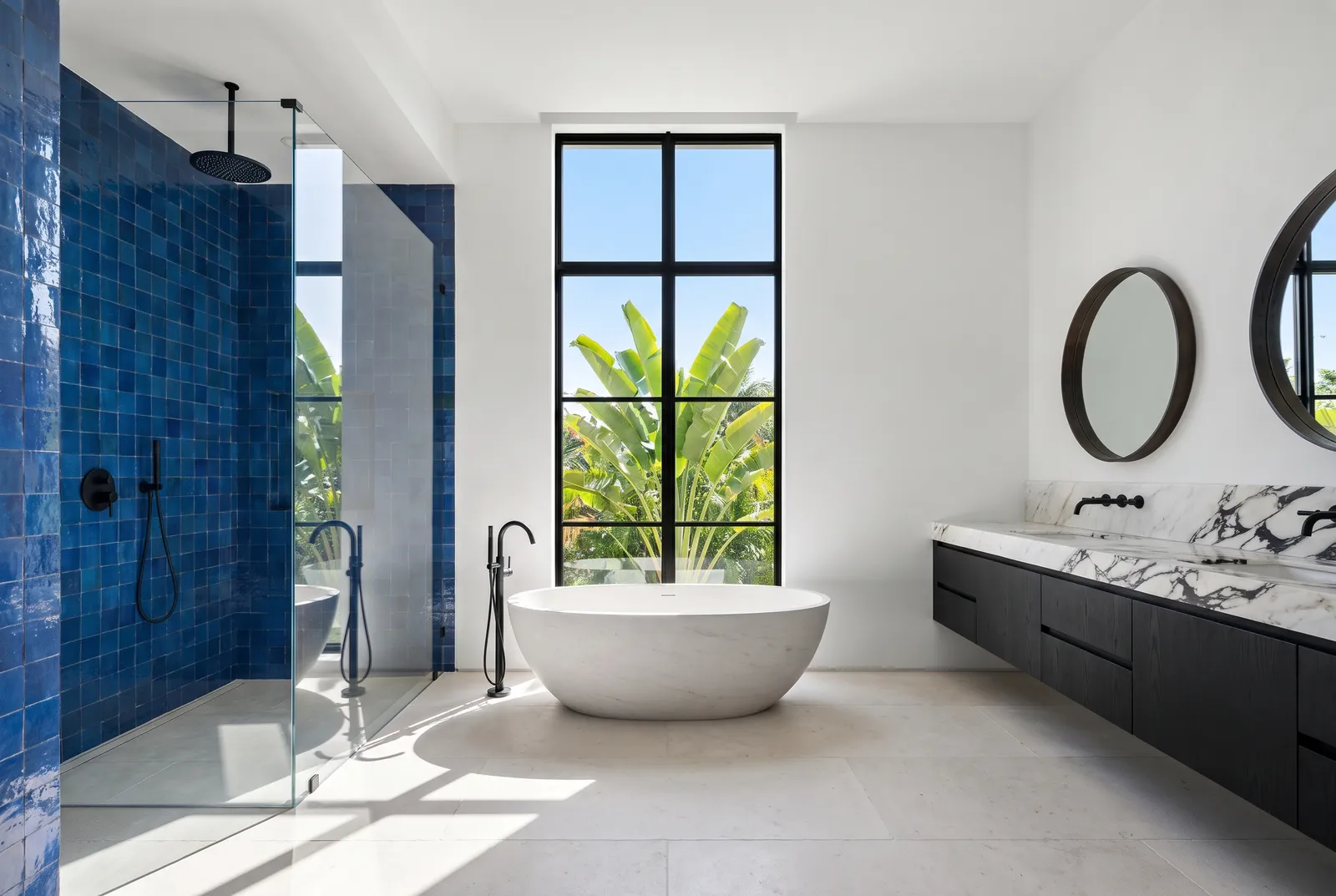After: a white bathroom with a cobalt zellige shower, a freestanding stone tub under a tall steel window and a charcoal oak vanity with a marble top.