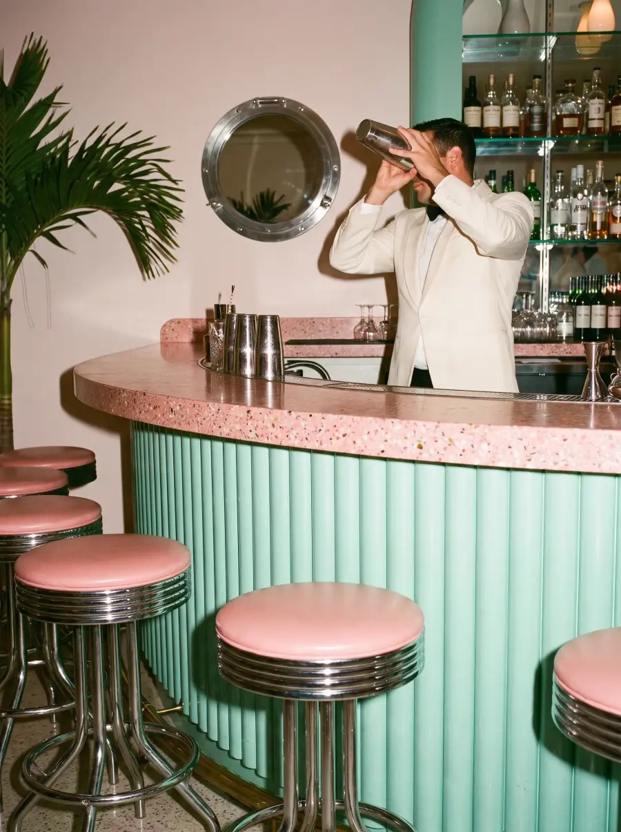 A bartender’s hands shaking a cocktail at the chrome and terrazzo bar