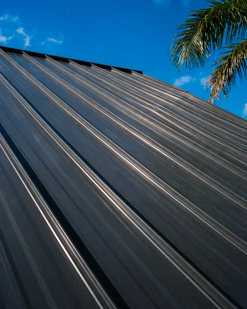 Looking up the slope of a charcoal standing-seam metal roof against a deep blue sky