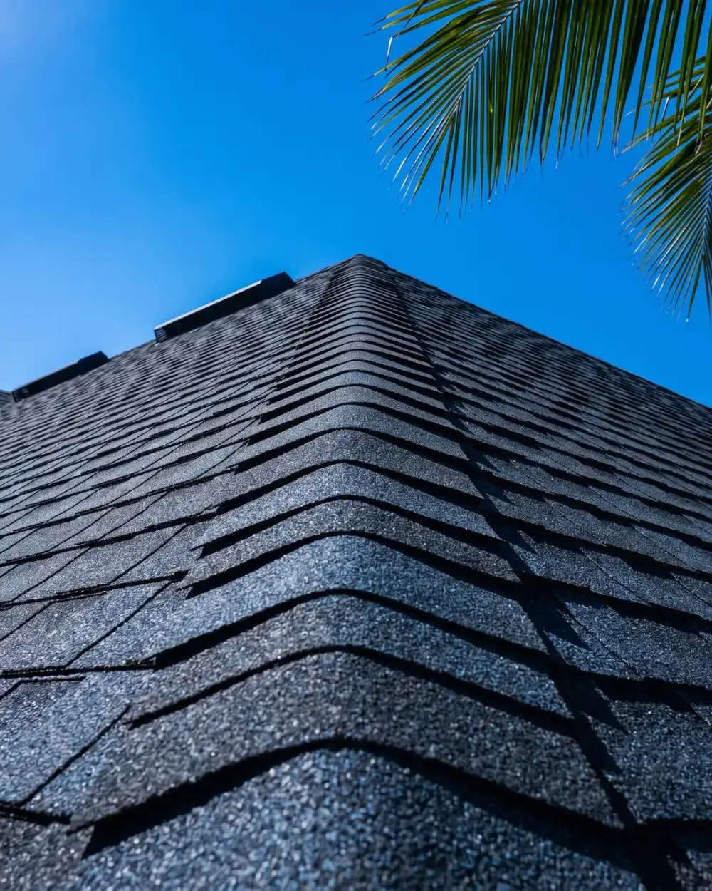 Looking up the hip of a slate-charcoal architectural shingle roof against a deep blue sky