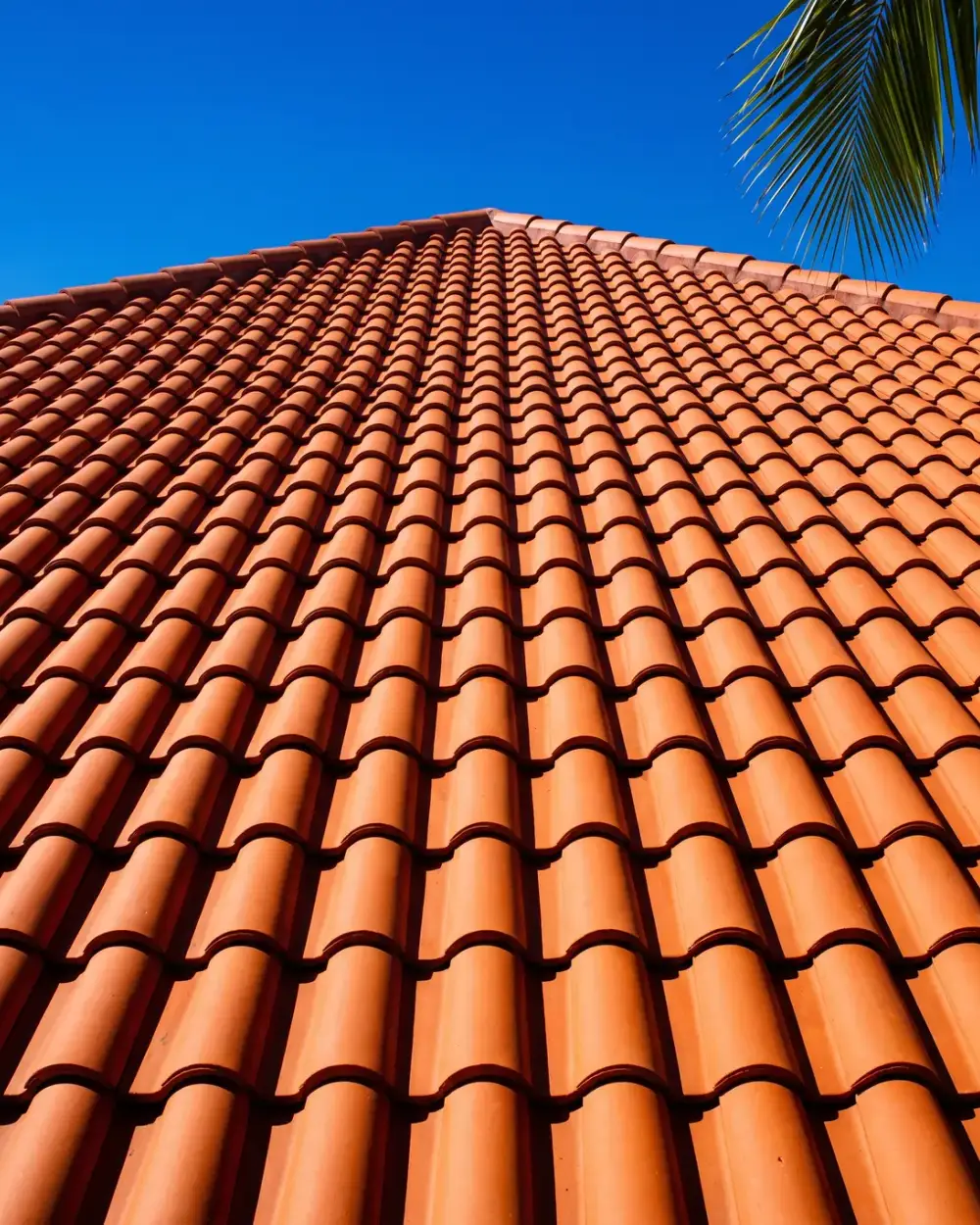 Looking up the slope of a terracotta clay barrel tile roof against a deep blue sky