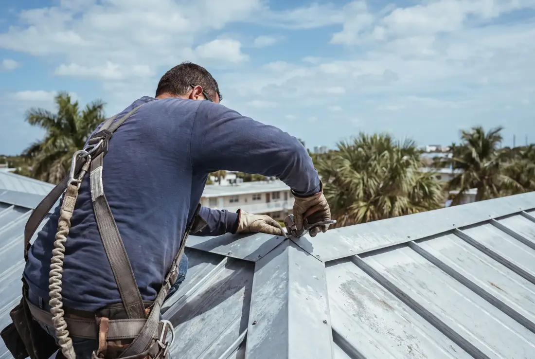 A roofer’s gloved hands seaming a standing-seam metal panel