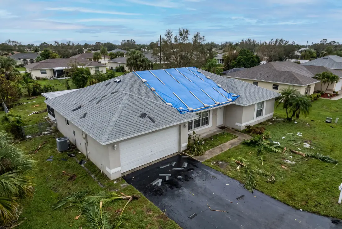 Aerial view of a roof with a blue emergency tarp secured over one slope