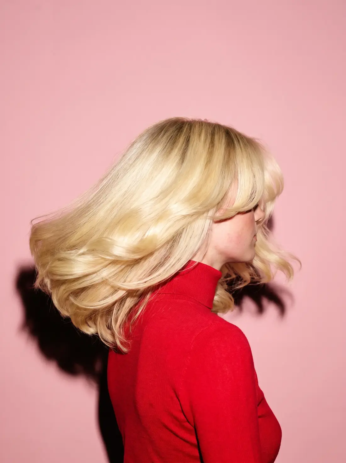 A bright blonde layered blowout caught mid-swing against a blush backdrop.