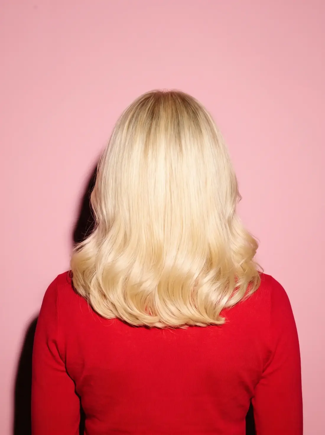 The same blonde blowout at rest from behind, full round curves sitting on the shoulders.